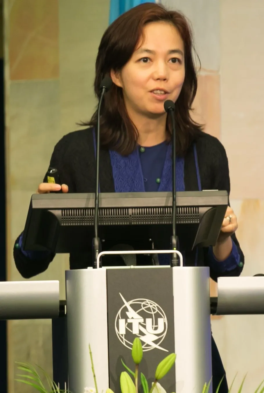 李飛飛站在講台後演講,面前有兩支麥克風